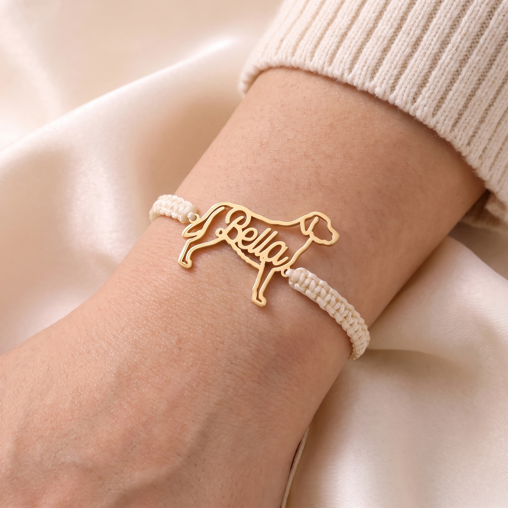 Gold pet name bracelet on an ivory braided cord, worn on a woman's wrist