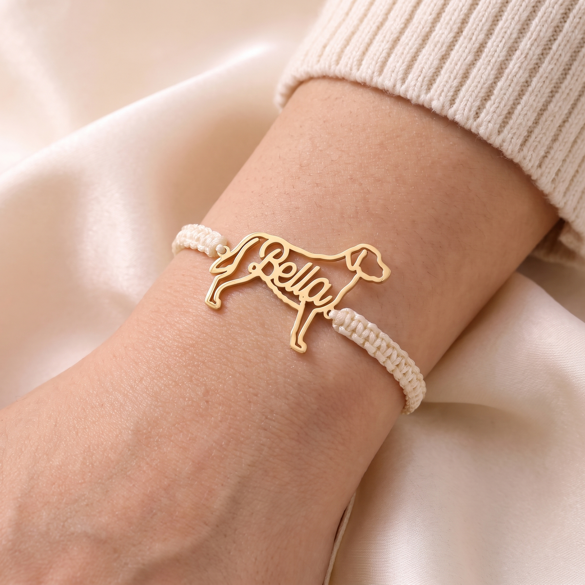 Gold pet name bracelet on an ivory braided cord, worn on a woman's wrist